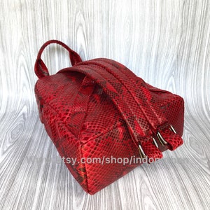 May include: Red leather backpack with a snakeskin pattern. The backpack has two adjustable straps and a zip closure.