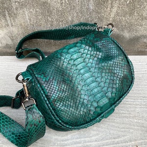 May include: A green snakeskin crossbody bag with a long adjustable strap. The bag has a flap closure and a silver buckle.
