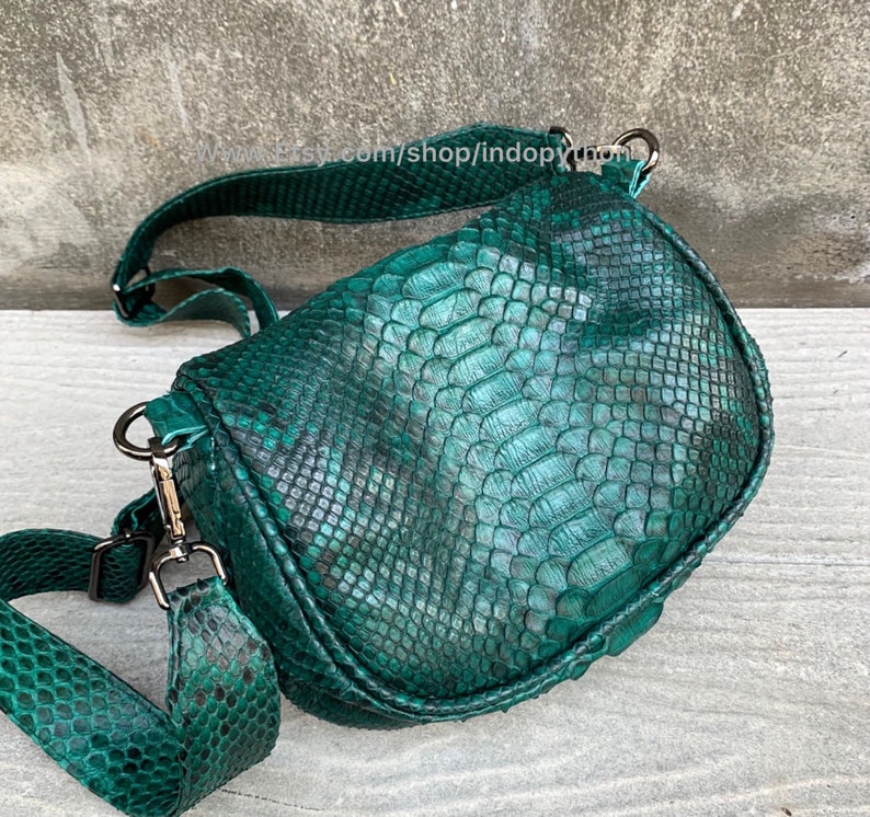 May include: A green snakeskin crossbody bag with a long adjustable strap. The bag has a flap closure and a silver buckle.