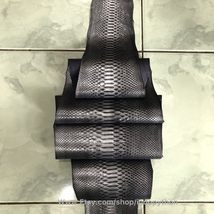May include: A stack of dark gray python leather hides. The hides are folded and have a textured, scaly surface.