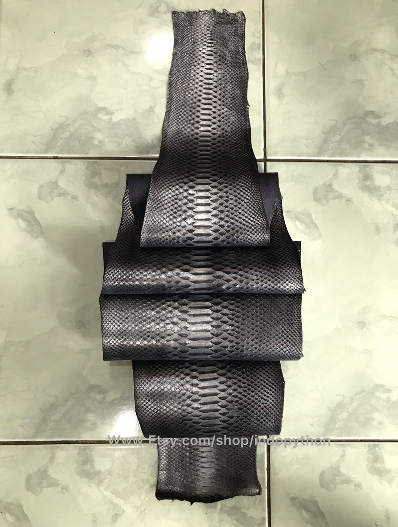 May include: A stack of dark gray python leather hides. The hides are folded and have a textured, scaly surface.