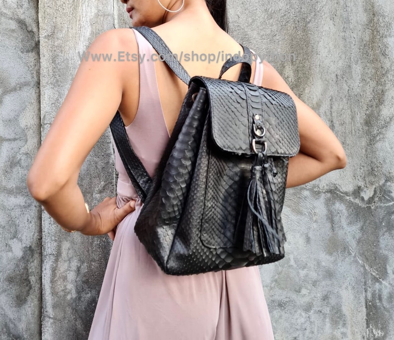 May include: A black leather backpack with a snakeskin pattern and a tassel. The backpack has a flap closure and a metal buckle.