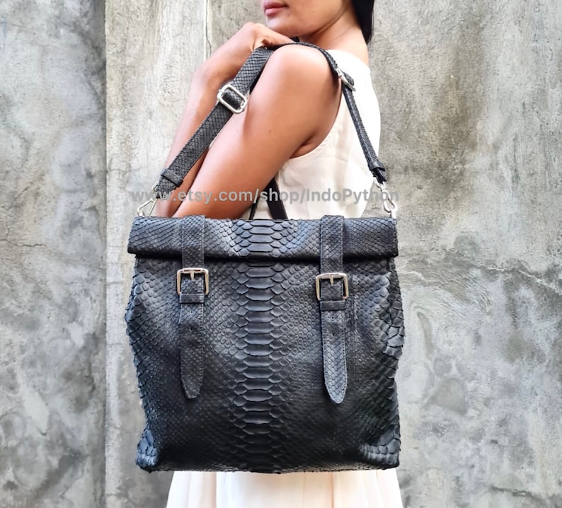 Peut inclure: Sac fourre-tout en cuir noir avec un motif en peau de serpent et des boucles argent&eacute;es. Le sac a une longue bandouli&egrave;re r&eacute;glable et un rabat.