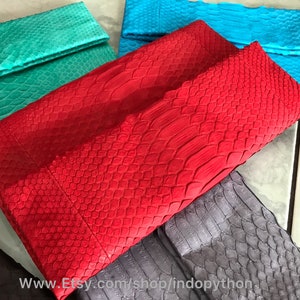 Peut inclure: Collection de pochettes color&eacute;es et textur&eacute;es. Les pochettes sont de diff&eacute;rentes nuances, dont le rouge, le turquoise et le bleu. La mati&egrave;re semble &ecirc;tre de la peau de serpent ou de reptile, avec un motif en &eacute;cailles. Les pochettes sont pli&eacute;es en haut.