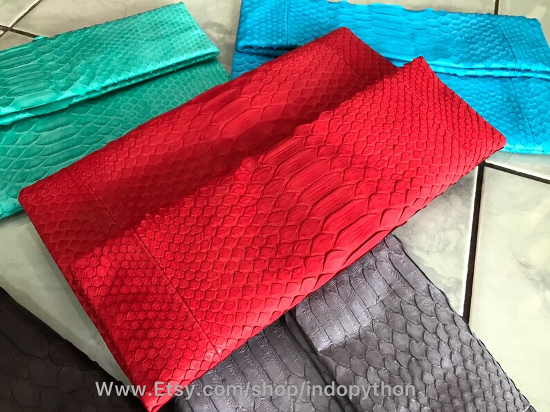 Peut inclure: Collection de pochettes color&eacute;es et textur&eacute;es. Les pochettes sont de diff&eacute;rentes nuances, dont le rouge, le turquoise et le bleu. La mati&egrave;re semble &ecirc;tre de la peau de serpent ou de reptile, avec un motif en &eacute;cailles. Les pochettes sont pli&eacute;es en haut.