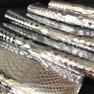 Op de afbeelding: Stapel zilveren python lederen vellen. Het leer heeft een textuur, schubbenpatroon. Het leer is glanzend en reflecterend.