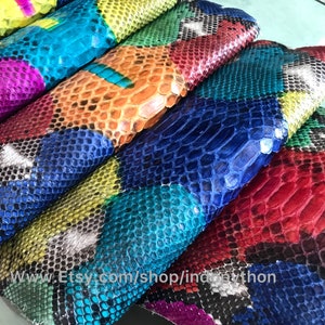 Op de afbeelding: Close-up van kleurrijk pythonhuid leer. Het leer is in vierkanten gesneden en in een patchwork-patroon gerangschikt. De kleuren omvatten rood, blauw, groen, geel en zwart.