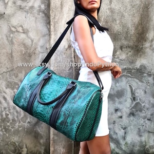 Puede incluir: Una bolsa de viaje de cuero de pitón verde con detalles en cuero negro y una correa de hombro negra. La bolsa tiene dos asas superiores y un cierre de cremallera. www.etsy.com/shop/IndoPython