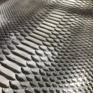 May include: Close-up of a silver snakeskin texture with a subtle gradient from dark to light. The scales are embossed and have a shiny finish.