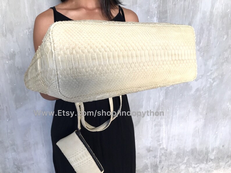 May include: A white python leather tote bag with a matching smaller clutch. The bag has a textured, snakeskin pattern.