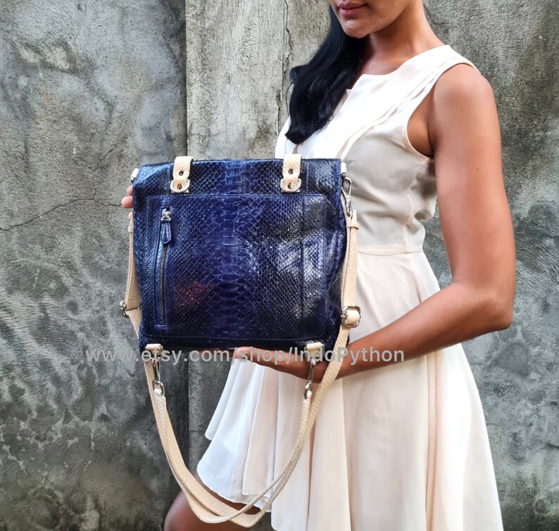 May include: A blue python leather tote bag with a beige shoulder strap. The bag has a zippered pocket on the front and silver hardware.