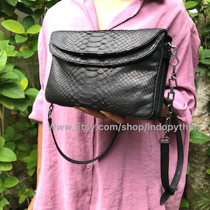 Może przedstawiać: Czarna skórzana torebka na ramię z klapką i łańcuszkowym paskiem. Torebka ma fakturowany wzór skóry węża i srebrny łańcuszkowy pasek.