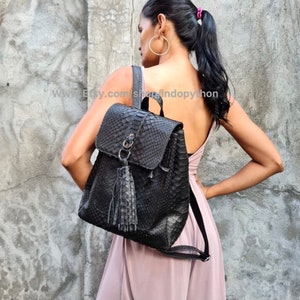 May include: Black leather backpack with a snakeskin pattern and a tassel. The backpack has a flap closure and a zipped pocket on the front.