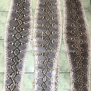 May include: Three long strips of light gray and brown python skin. The skin has a textured pattern of scales.