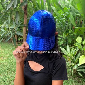 May include: A blue baseball cap with a snakeskin pattern. The cap has a curved brim and a structured crown.