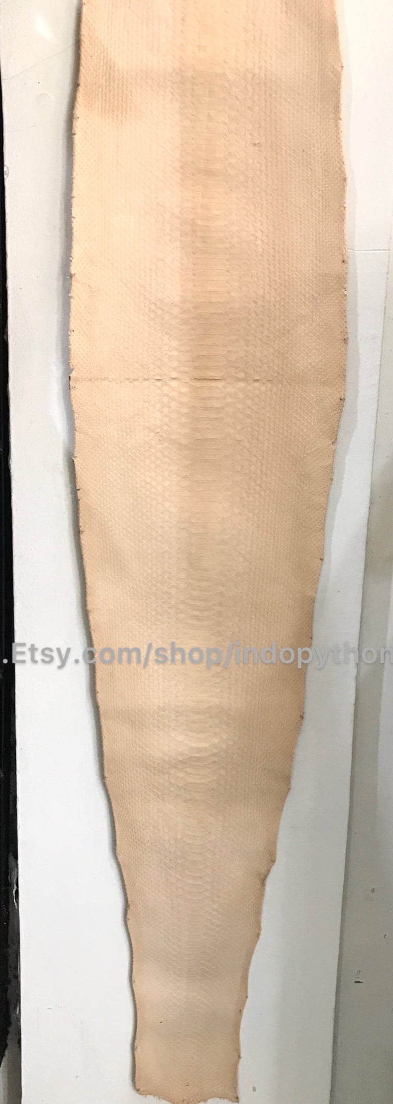 Puede incluir: Una sola pieza de piel de pit&oacute;n de color beige claro con un patr&oacute;n texturizado en forma de escamas. La piel es alargada e irregular, con un aspecto natural y org&aacute;nico. La URL de la tienda Etsy es visible.