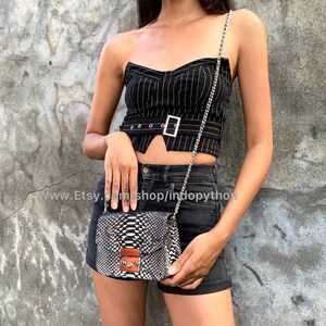 May include: A black and white striped strapless top with a silver buckle belt. The top is paired with black denim shorts and a small silver chain bag with a snakeskin pattern.
