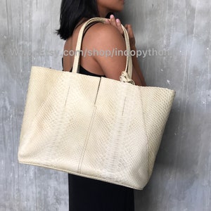 May include: A large, off-white tote bag made of python skin. The bag has a top zipper closure and two top handles.