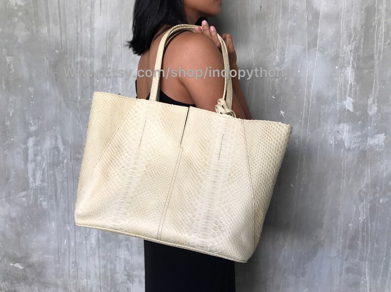 May include: A large, off-white tote bag made of python skin. The bag has a top zipper closure and two top handles.