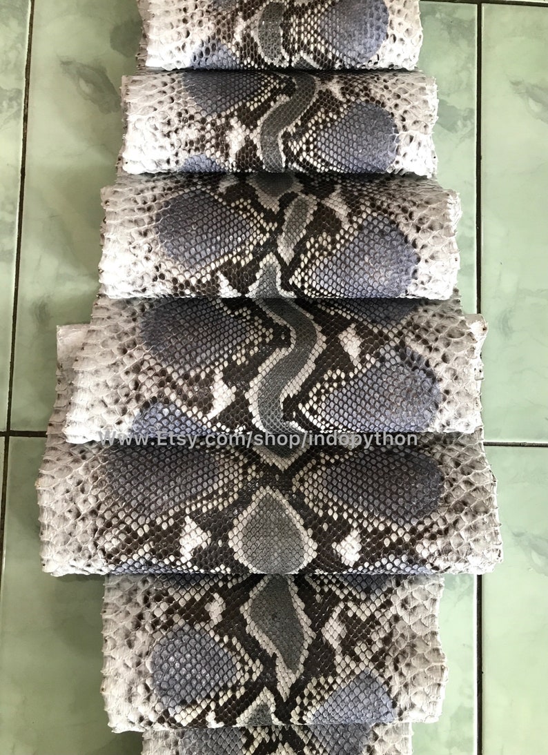 May include: A stack of gray and black python skins with a white background. The skins are arranged in a staggered pattern, with the top skin being the largest and the bottom skin being the smallest. The skins are all smooth and have a natural, textured pattern.