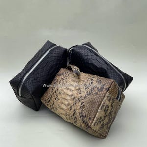 May include: Three different-colored snakeskin cosmetic bags. The bags are all rectangular and have a zipper closure. The bag in the front is a light brown color, while the two bags in the back are black.