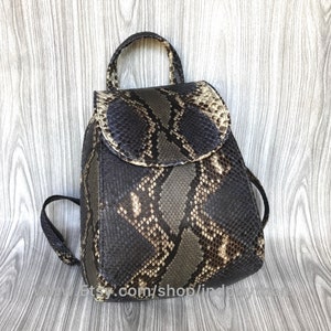 Könnte beinhalten: Ein kleiner Rucksack aus schwarzem und braunem Schlangenleder mit Klappenverschluss und verstellbaren Trägern.