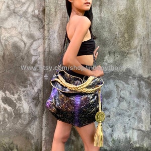 Op de afbeelding: Een paarse en gouden pythonleren tote bag met een gouden kwast. De tas heeft een gevlochten band en een gouden muntbedel.