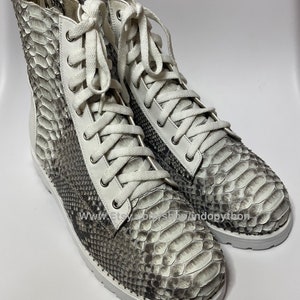 May include: White leather high-top boots with white laces and a snakeskin pattern. The boots have a white rubber sole.