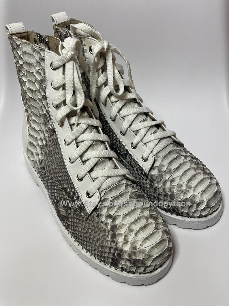 May include: White leather high-top boots with white laces and a snakeskin pattern. The boots have a white rubber sole.