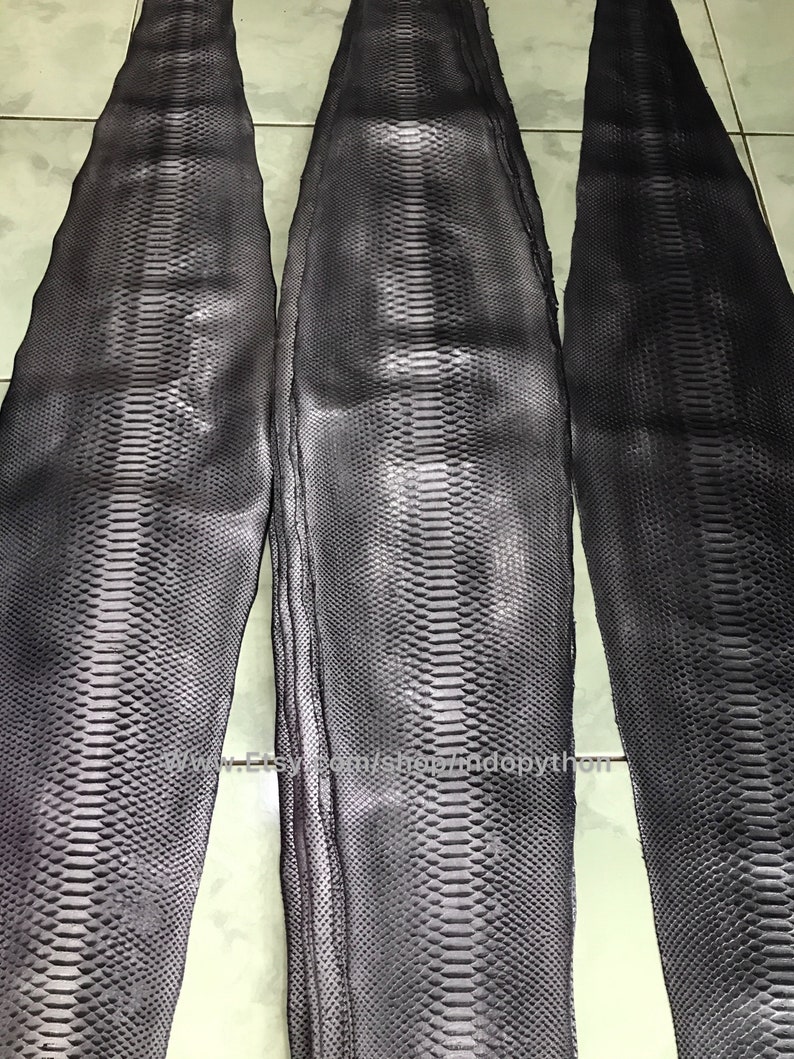 May include: Three pieces of dark gray python skin, each with a unique pattern of scales. The skin is smooth and supple, and it would be ideal for use in leather goods.