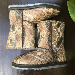 Op de afbeelding: Een paar bruine en zwarte slangenleren laarzen met een zwarte zool. De laarzen zijn gemaakt van echt slangenleer en hebben een uniek patroon.