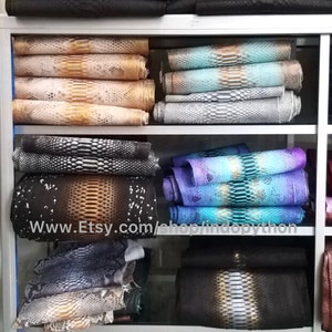 Może przedstawiać: P&oacute;łka z ekspozycją r&oacute;żnych sk&oacute;r pytona w r&oacute;żnych kolorach i wzorach. Sk&oacute;ry są ułożone na p&oacute;łkach i są dostępne do kupienia. Adres strony internetowej www.Etsy.com/shop/indopython jest widoczny na p&oacute;łce.