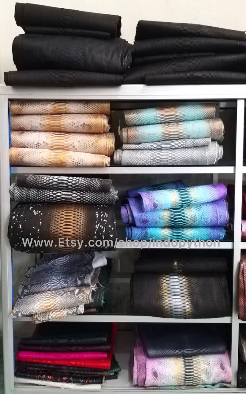 Może przedstawiać: P&oacute;łka z ekspozycją r&oacute;żnych sk&oacute;r pytona w r&oacute;żnych kolorach i wzorach. Sk&oacute;ry są ułożone na p&oacute;łkach i są dostępne do kupienia. Adres strony internetowej www.Etsy.com/shop/indopython jest widoczny na p&oacute;łce.