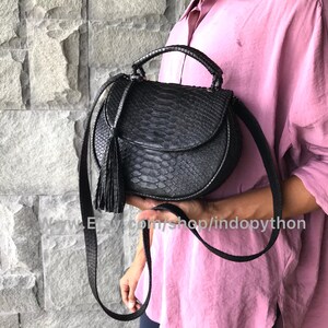 May include: A black leather handbag with a snakeskin pattern and a tassel. The bag has a top handle and a long strap for carrying on the shoulder.
