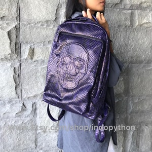 Może przedstawiać: Purpurowy skórzany plecak z wzorem czaszki. Plecak ma zamek błyskawiczny i regulowane paski.