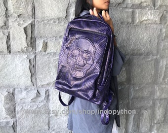 May include: A purple leather backpack with a skull design. The backpack has a zipper closure and adjustable straps.