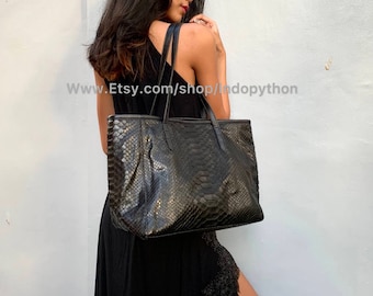 Könnte beinhalten: Eine schwarze Ledertasche mit Schlangenhautmuster. Die Tasche hat zwei obere Henkel und einen Reißverschluss.