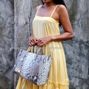 May include: A woman wearing a yellow dress is holding a grey and white python skin tote bag. The bag has a top handle and a shoulder strap. The text "www.etsy.com/shop/IndoPython" is visible on the bag.