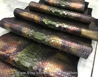 May include: Several pieces of iridescent green, brown, and gold python skin leather. The leather has a scaly texture and is arranged in a stack.