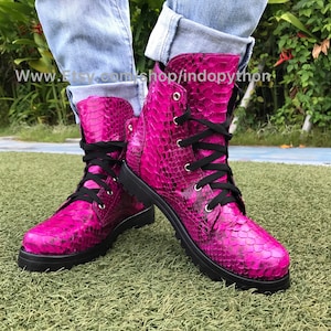 May include: Pink snakeskin boots with black laces. The boots have a chunky sole and are made of real leather.