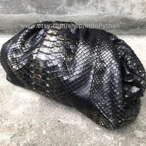 May include: A black clutch bag made from python skin with a gold metallic finish.