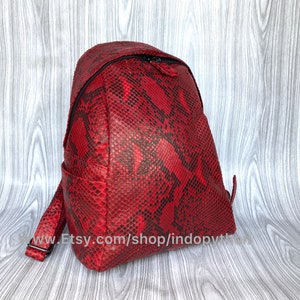 May include: A red snakeskin backpack with a black zipper and adjustable straps. The backpack is made of genuine leather and has a unique, textured design.