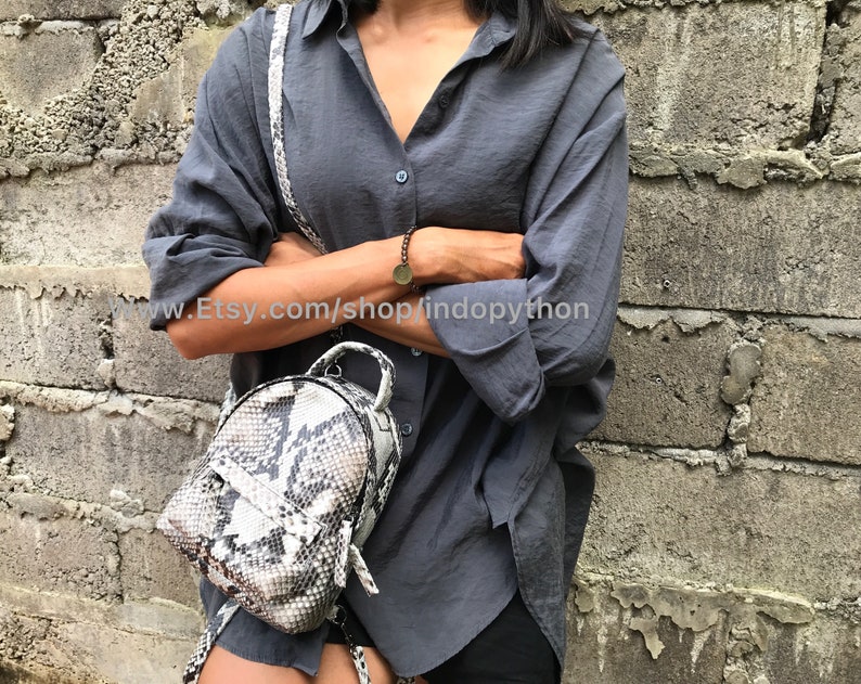K&ouml;nnte beinhalten: Ein kleiner, runder Rucksack aus wei&szlig;er und schwarzer Schlangenhaut mit Rei&szlig;verschluss. Der Rucksack wird von einer Person getragen, die ein graues Hemd und eine schwarze Hose tr&auml;gt. Der Text "www.Etsy.com/shop/indopython" ist im Bild sichtbar.