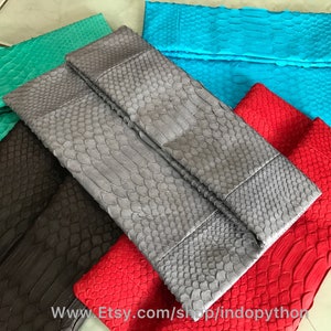 May include: Five different colored python skin clutches. The clutches are folded in half and are arranged in a pile. The colors are teal, gray, black, red, and green.
