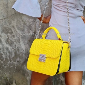 Può includere: Una borsa a mano in pelle di serpente giallo brillante con una tracolla a catena argentata e una chiusura a lucchetto argentata. La borsa ha un bordo nero attorno ai bordi. Il testo "www.Etsy.com/shop/Andopython" è visibile nell'immagine.