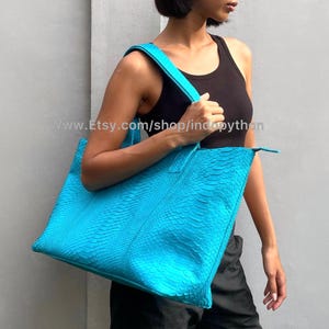 May include: A bright turquoise tote bag made of python leather. The bag has a top zipper closure and two handles.