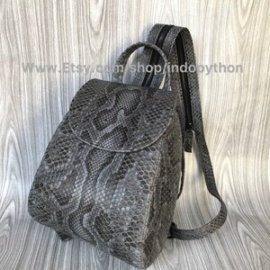 K&ouml;nnte beinhalten: Ein grauer Schlangenleder-Rucksack mit Rei&szlig;verschluss und verstellbaren Tr&auml;gern. Der Rucksack hat eine kleine, abgerundete Form und eine strukturierte Oberfl&auml;che. www.Etsy.com/shop/indopython