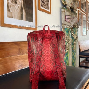 May include: Red python skin backpack with adjustable straps. The backpack is made of genuine python skin and has a unique, textured pattern.
