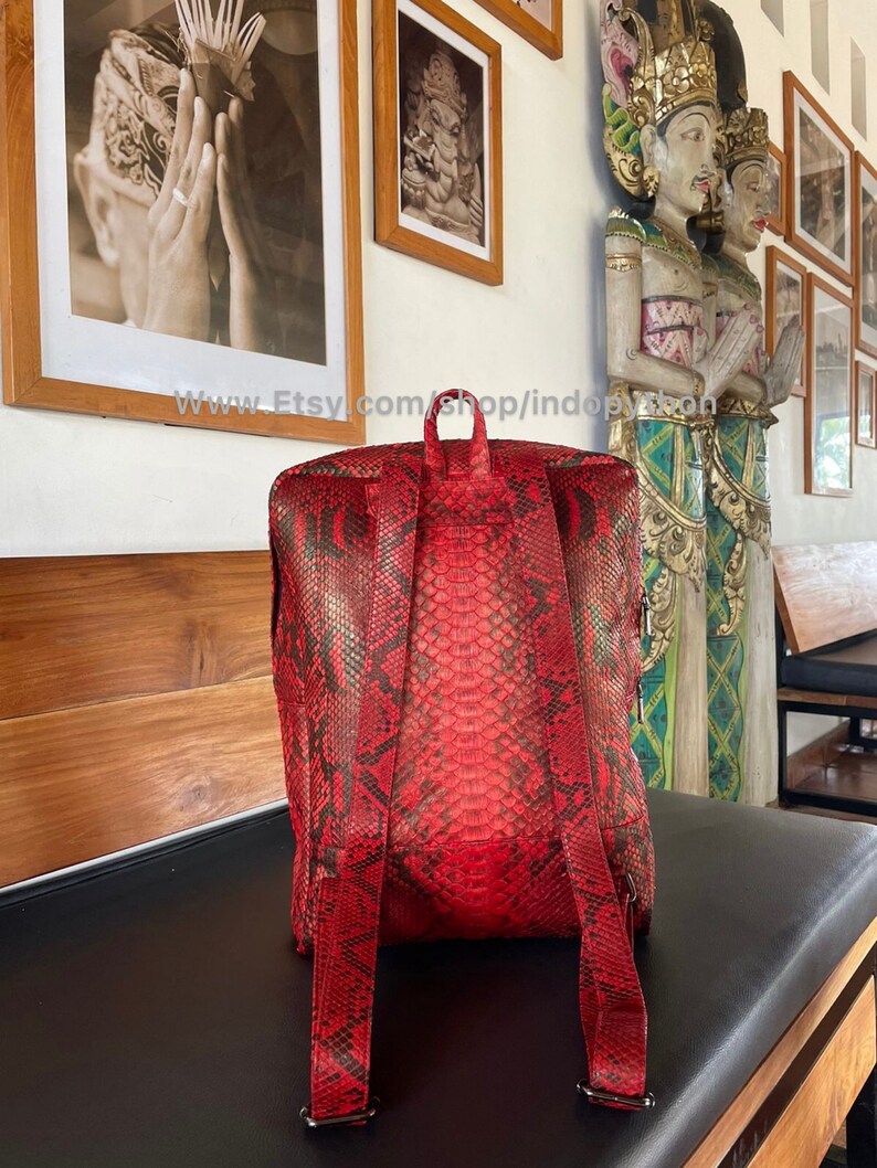 May include: Red python skin backpack with adjustable straps. The backpack is made of genuine python skin and has a unique, textured pattern.