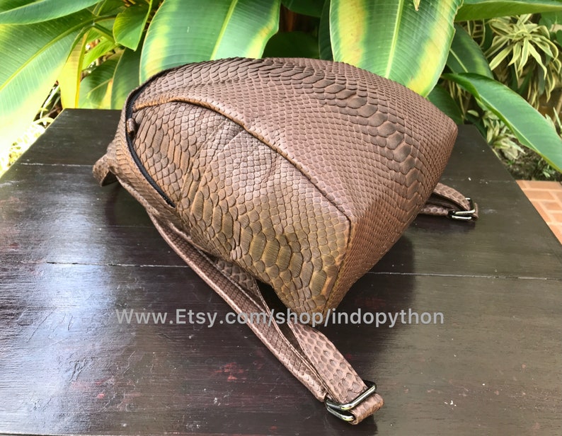 May include: A brown backpack with a snakeskin pattern. The bag has adjustable straps and a zipper closure. The Etsy shop URL is visible at the bottom of the image.